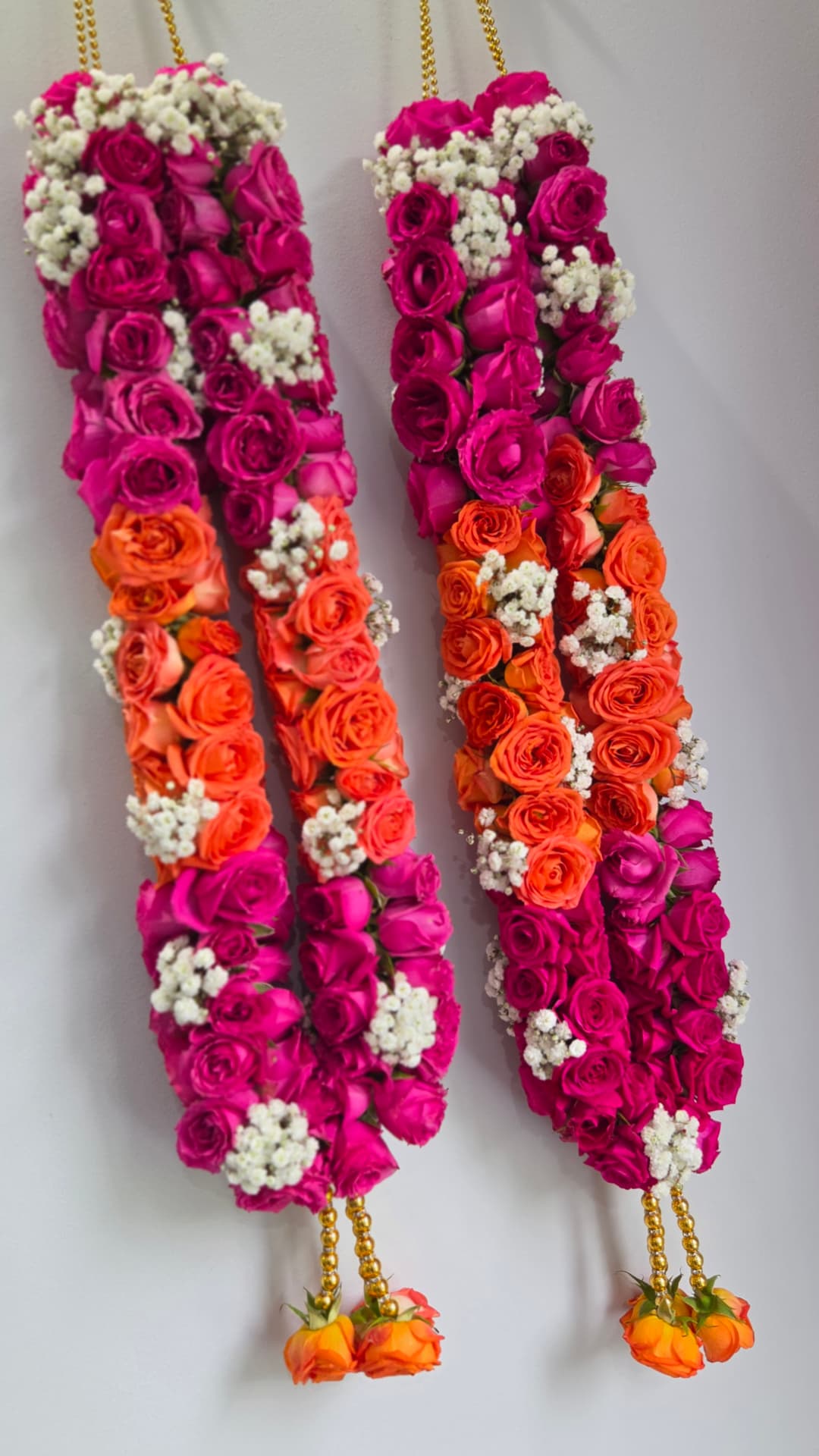 Vibrant pink and orange rose wedding garland pair with baby's breath and gold tassels
