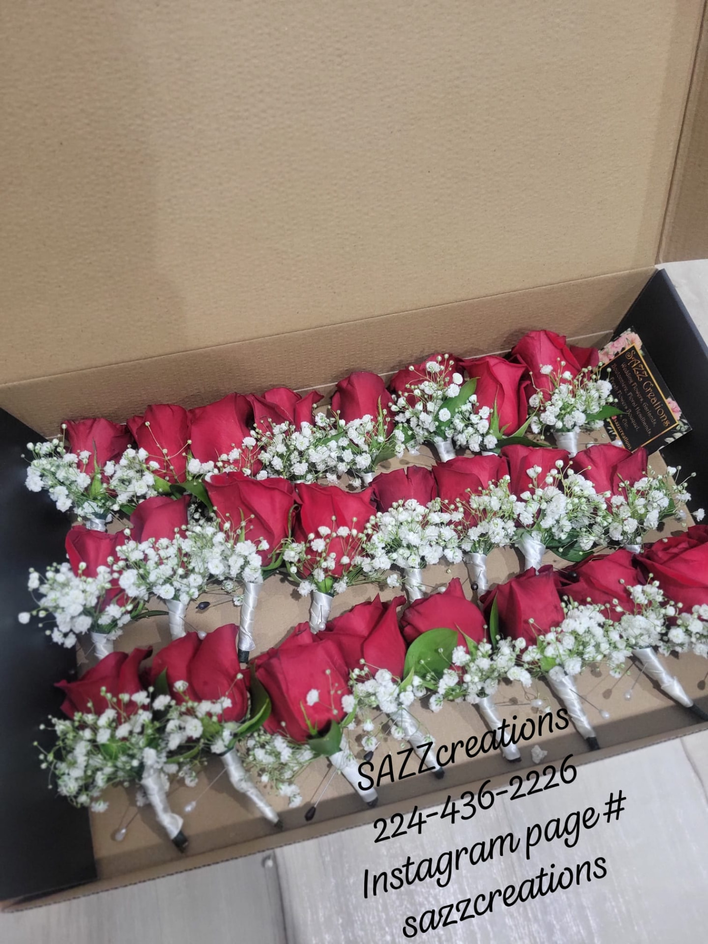 Red rose boutonnieres with baby's breath and white ribbon arranged in a large gift box